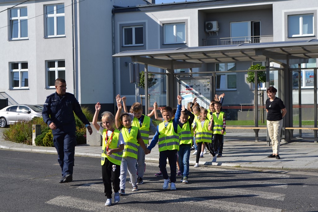 Policjan pokazuje pierwszakom jak prawidłowo przechodzić przez pasy