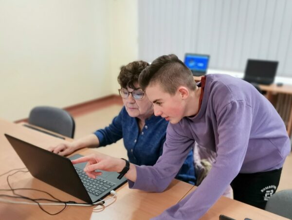 Uczeń pomaga Słuchaczce Uniwersytetu Trzeciego Wieku w wykonywaniu zadania komputerowego