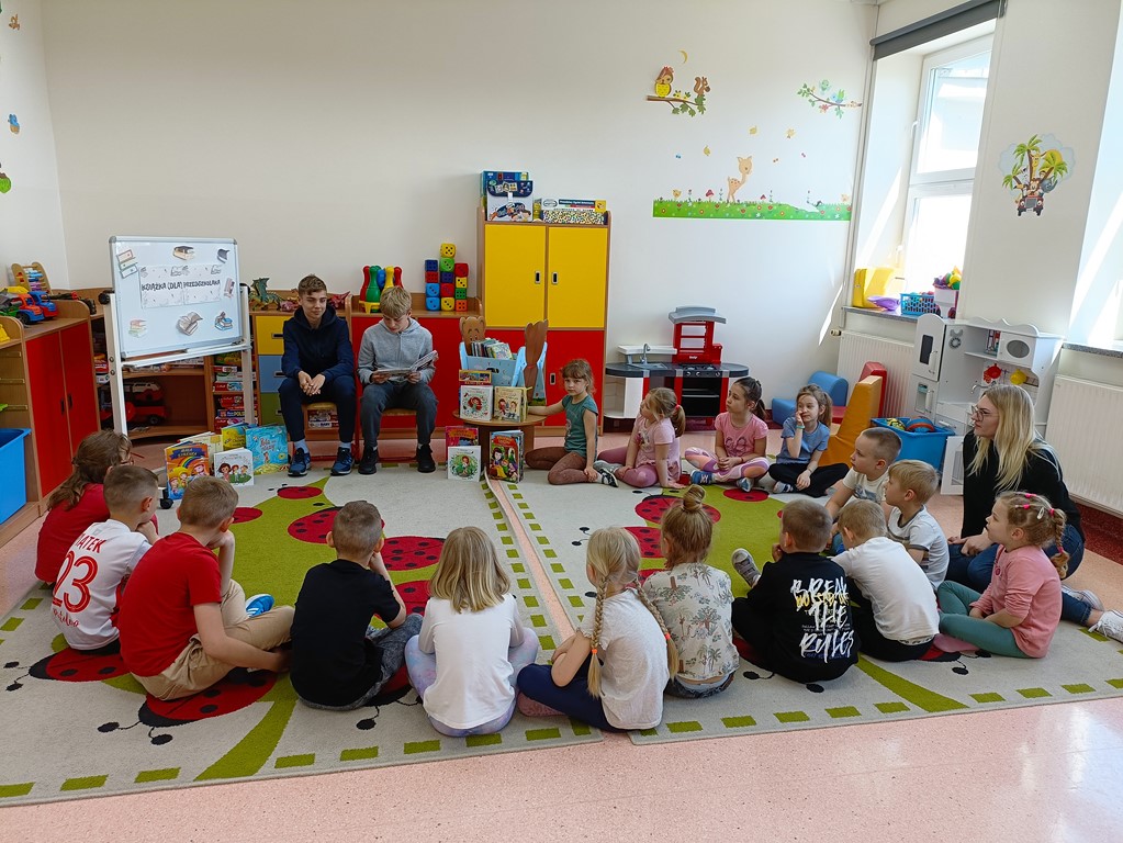 Uczniowie z klasy ósmej czytają książkę swoim młodszym kolegom